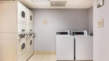 Une buanderie équipée de deux machines à laver et deux sèche-linge à chargement frontal, d’une horloge murale et d’un panneau indiquant la durée des cycles de lavage.