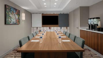 Una sala de conferencias con una larga mesa, sillas, un televisor y un dispensador de agua.