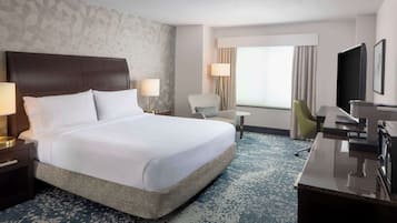 A hotel room with a large bed, a desk, a chair, a TV, and a window with curtains.