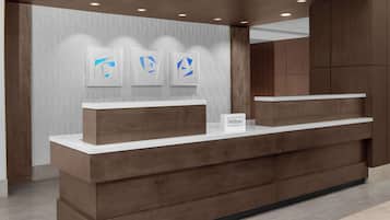 A modern reception desk with a wooden finish and a white countertop. There are three framed artworks above the desk and a sign that reads "Hilton Honors".