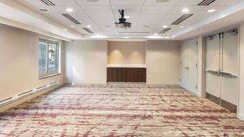 A spacious hotel room with a patterned carpet, a projector ceiling, and a large window on the left.