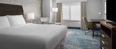 A hotel room with a large bed, a desk, a chair, a TV, and a window with curtains.