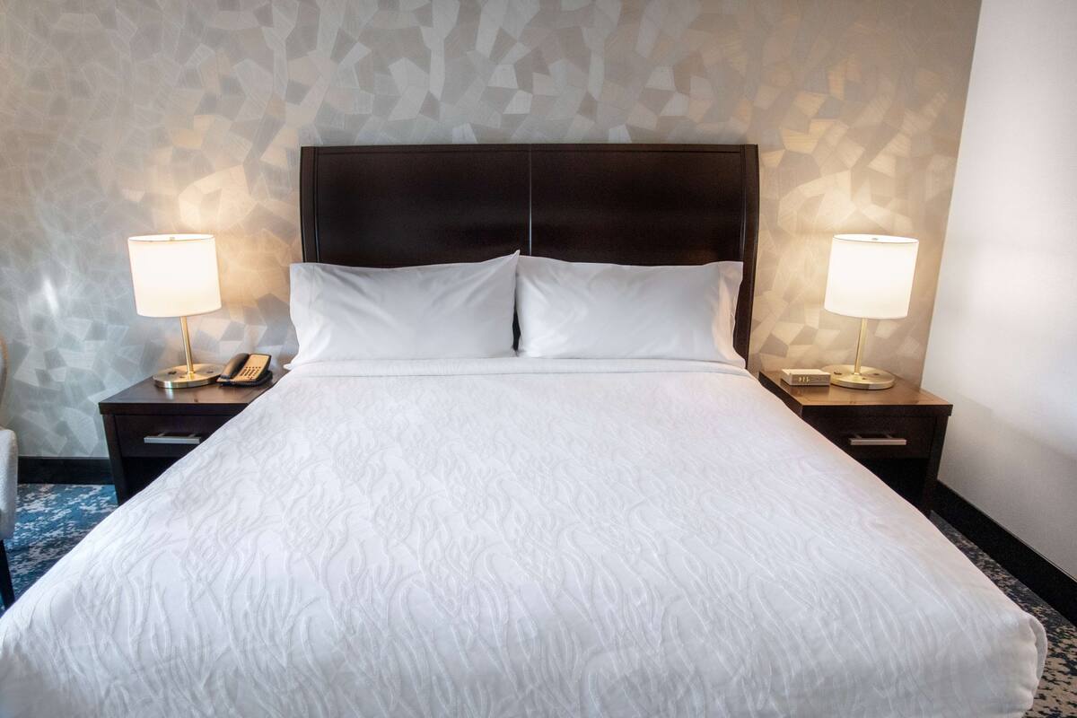 A neatly made bed with a dark headboard, two bedside tables with lamps, and a patterned wall.