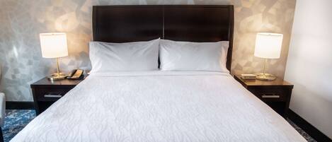 A neatly made bed with a dark headboard, two bedside tables with lamps, and a patterned wall.