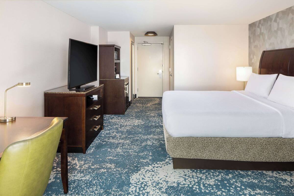 A hotel room with a bed, a television, a desk with a lamp, and a wardrobe.