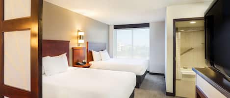 A hotel room with two beds, a TV, a bathroom with a bathtub, and a city view.