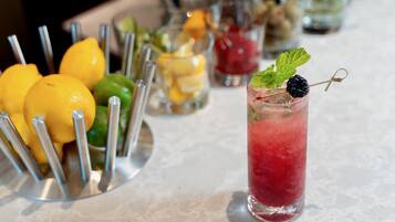 A bar area with a variety of drinks, including a tall glass with a red beverage and a blackberry garnish, and a metal tray with lemons and limes.