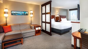 Une chambre d’hôtel avec un canapé, un lit, une table de chevet, une petite table et une fenêtre donnant sur la ville.
