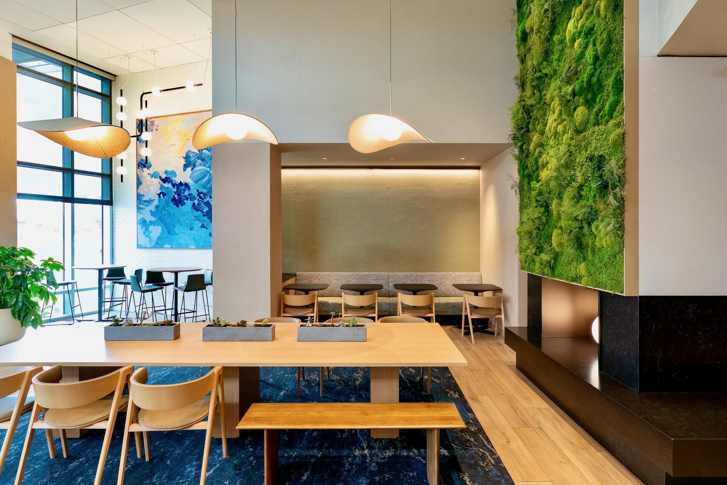 A modern reception area with a long wooden reception desk, multiple chairs, and a green vertical garden wall.