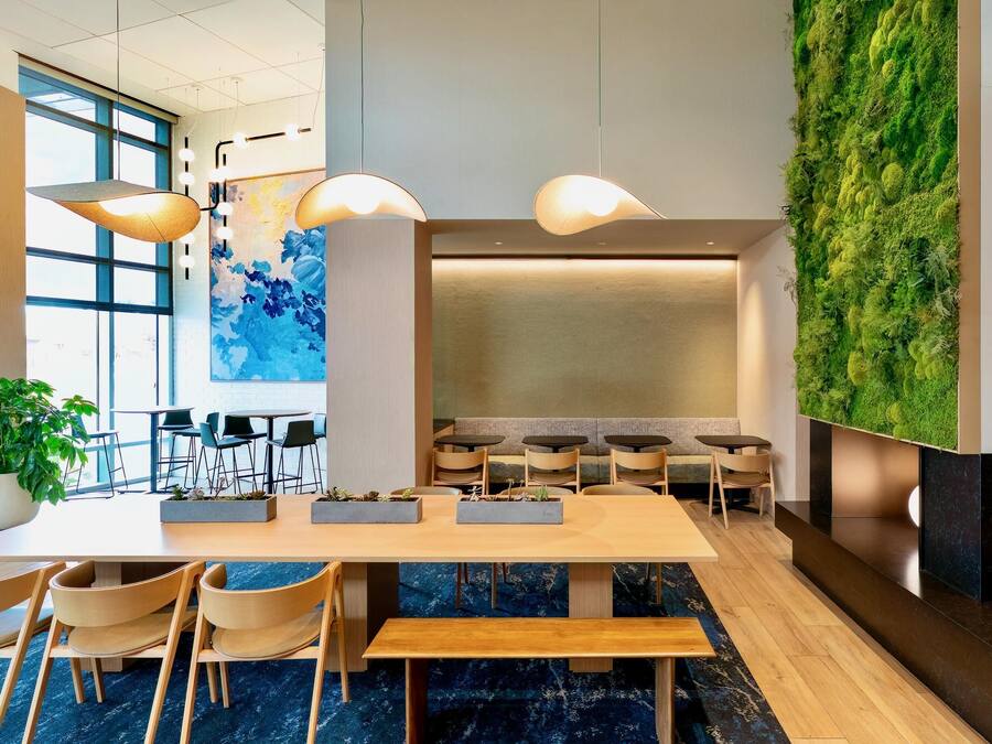 A modern reception area with a long wooden reception desk, multiple chairs, and a green vertical garden wall.