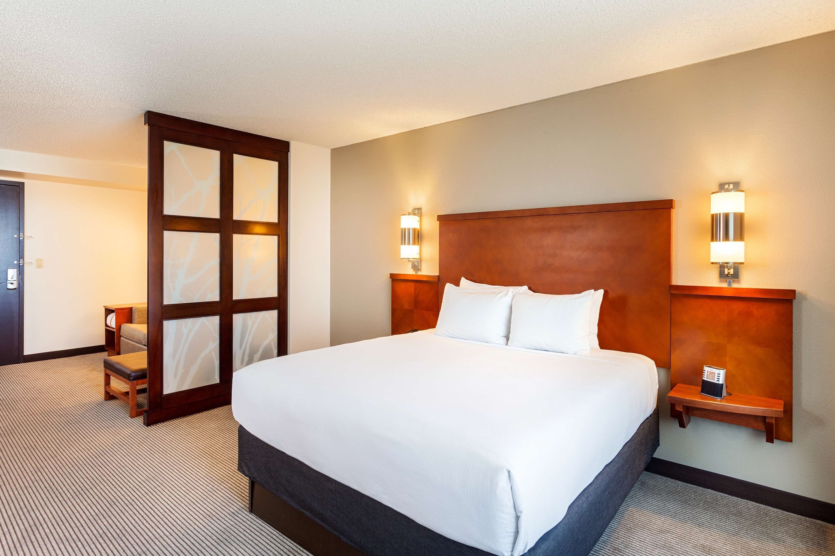 Hotelkamer met een groot bed, twee nachtkastjes, een stoel en een schuifdeur.