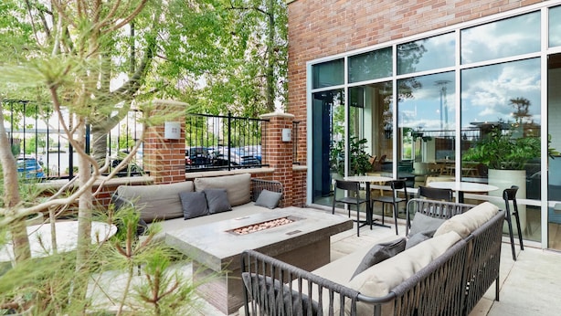 Une terrasse extérieure avec un mur en briques, de grandes fenêtres et des meubles d’extérieur, notamment un canapé et des fauteuils.