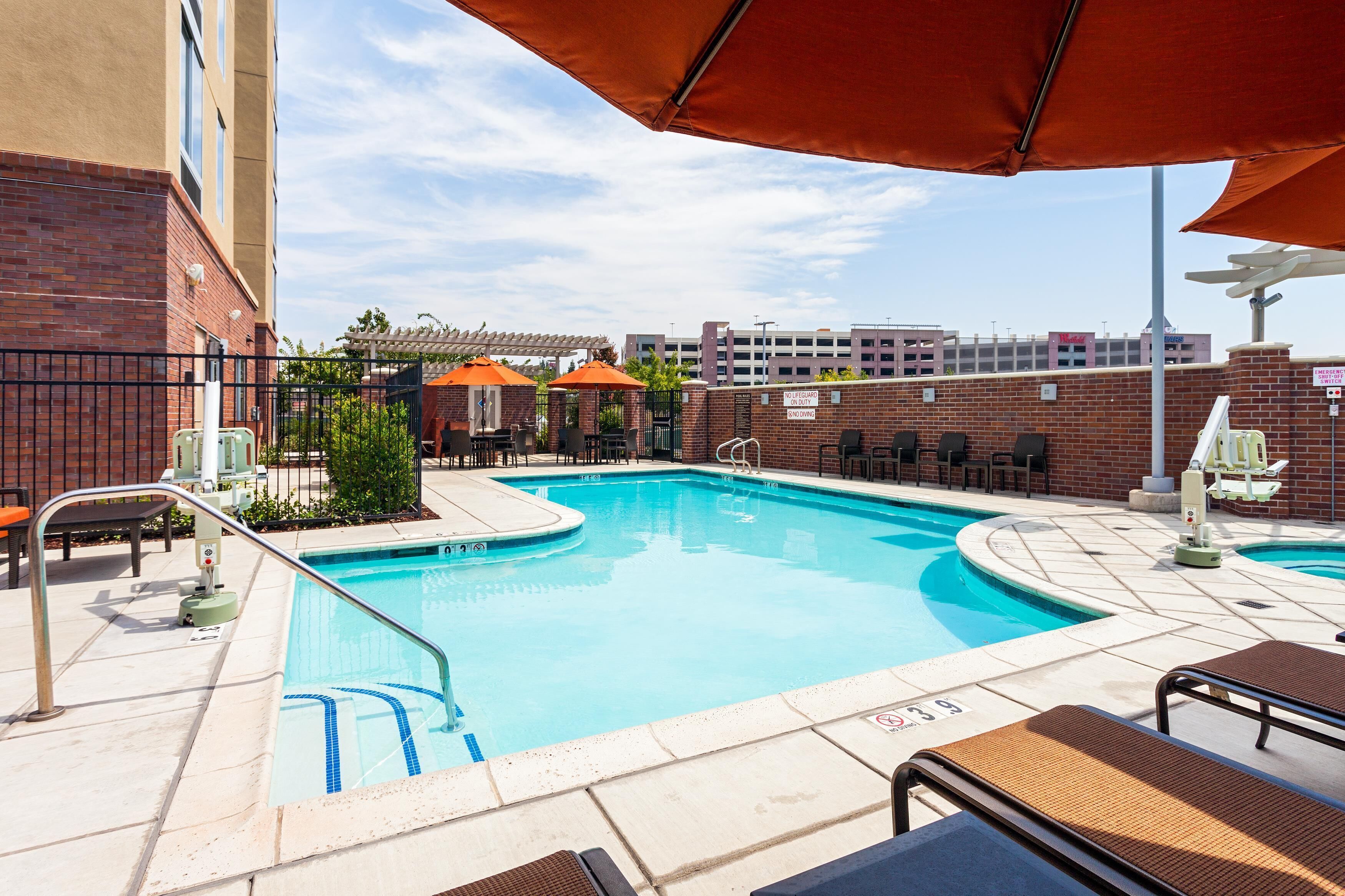 A swimming pool with lounge chairs and umbrellas, surrounded by brick walls and a covered patio area.