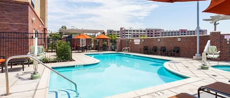 A swimming pool with lounge chairs and umbrellas, surrounded by brick walls and a covered patio area.