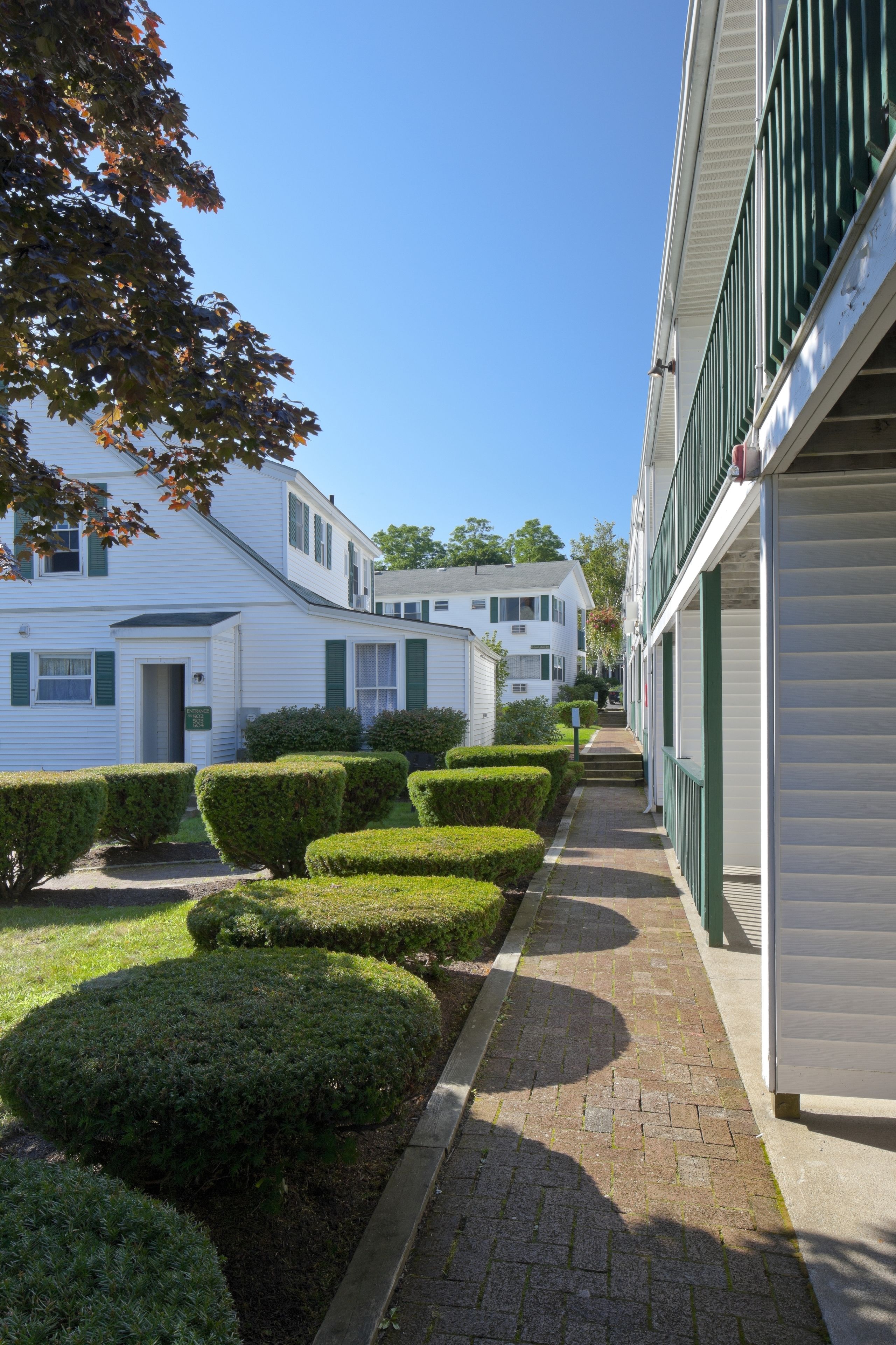 Une rangée de maisons mobiles blanches aux volets verts, un chemin pavé et des haies bien entretenues.