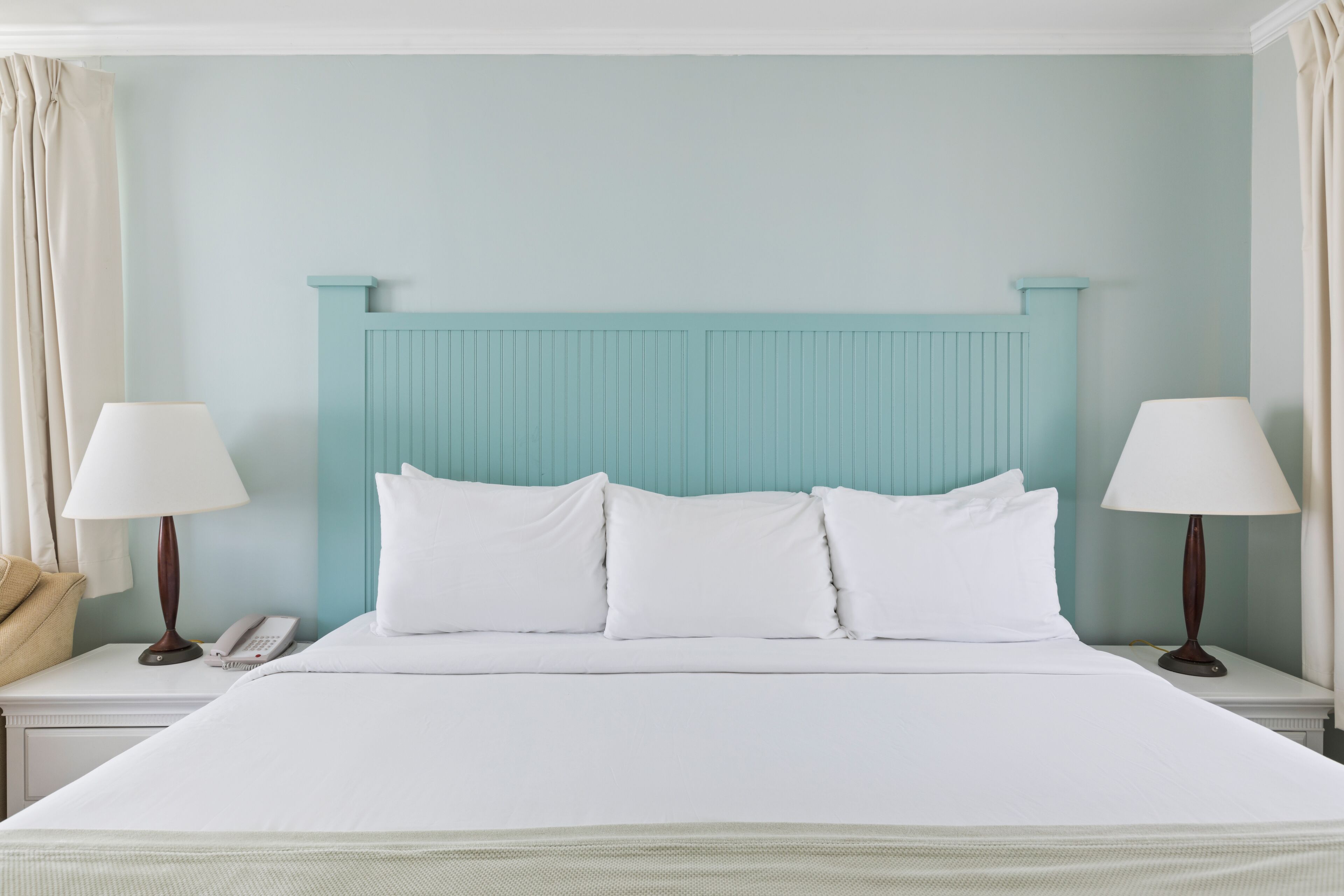 Una cama bien hecha con sábanas blancas, un cabecero azul claro y dos lámparas de noche.