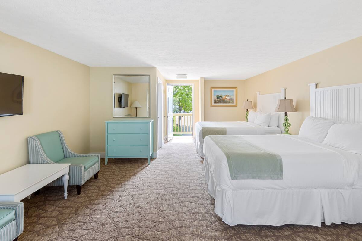 A hotel room with two beds, a desk, a chair, a dresser, and a TV.
