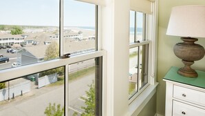 Habitación con vista a la playa y al estacionamiento, una lámpara en una cómoda y una ventana con persianas.