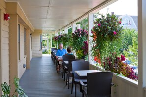 A covered outdoor seating area with tables and chairs, surrounded by potted plants and flowers. - The Colonial Inn (Ogunquit)