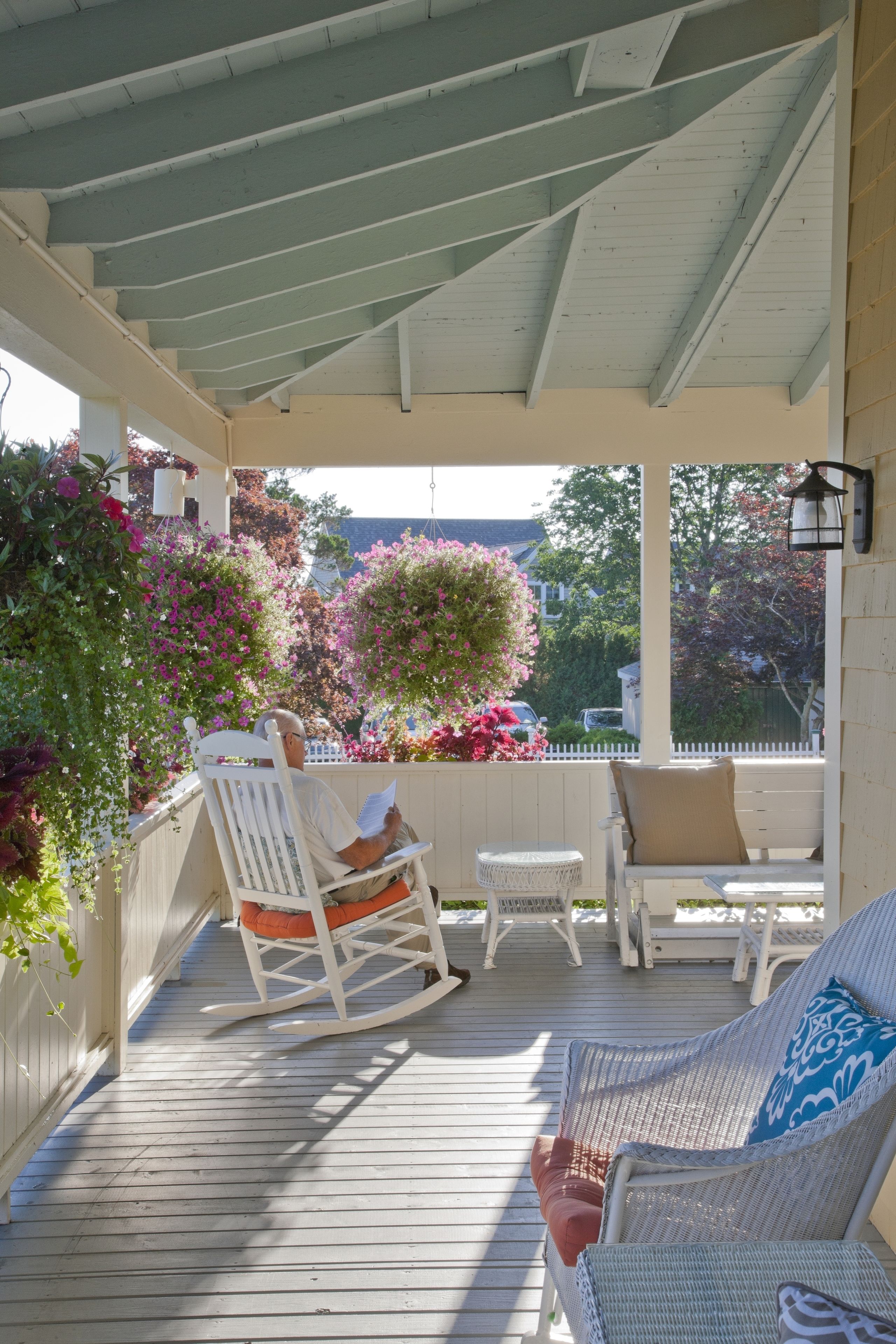 A covered porch with rocking chairs and a table, surrounded by potted plants and flowers.