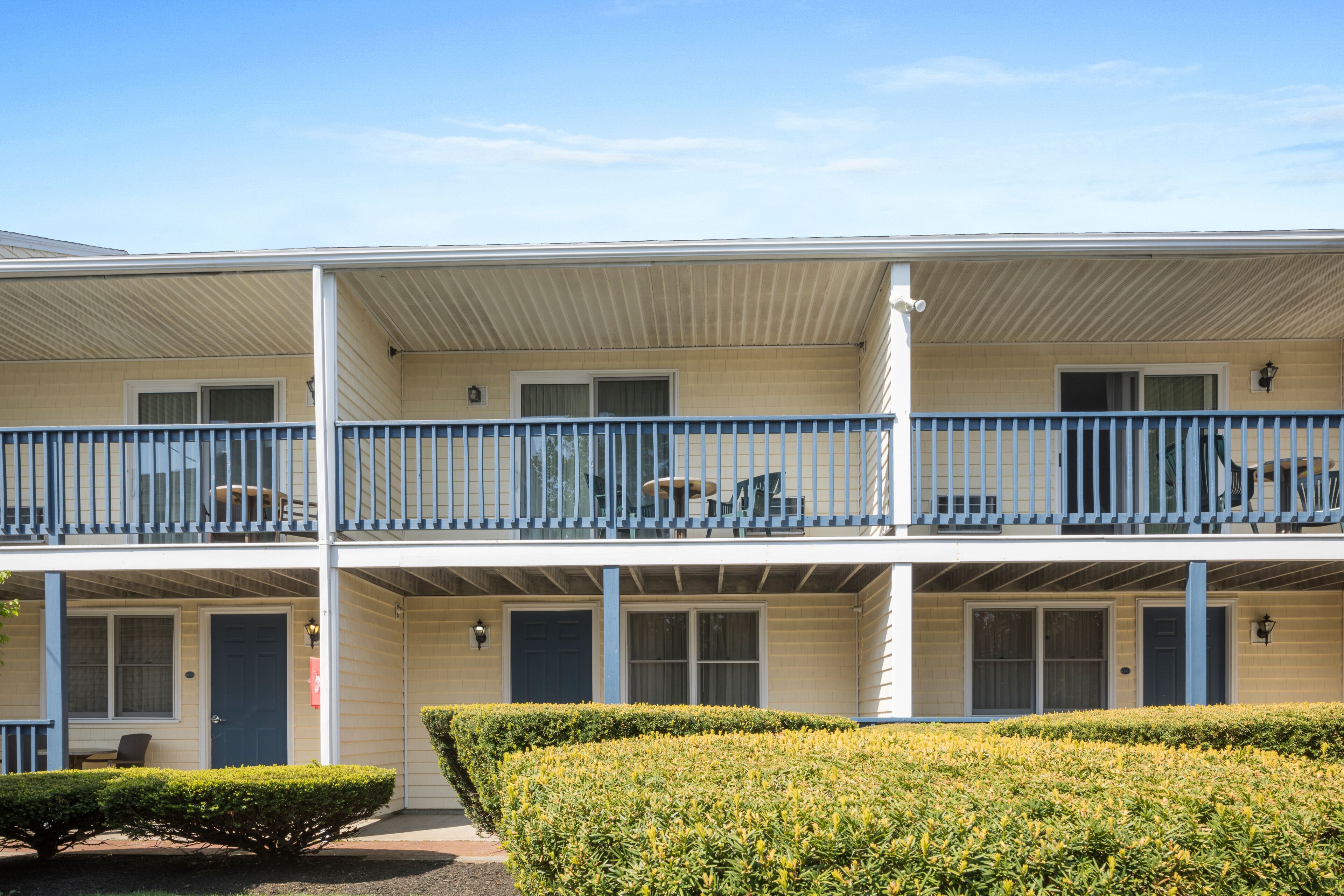 A two-story motel with a covered balcony, a small front porch, and a well-maintained hedge.