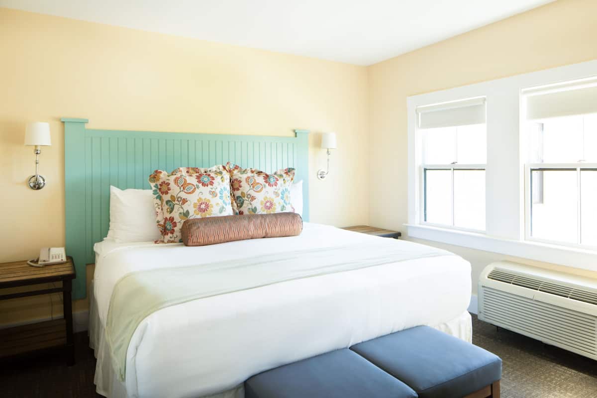 A neatly made bed with floral pillows, a teal headboard, and a bedside table with a lamp.
