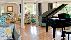 Un amplio salón con un piano de cola, asientos cómodos y ventanas grandes.