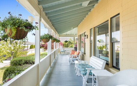 A covered porch with white wicker furniture, hanging flower baskets, and a view of the surrounding greenery.