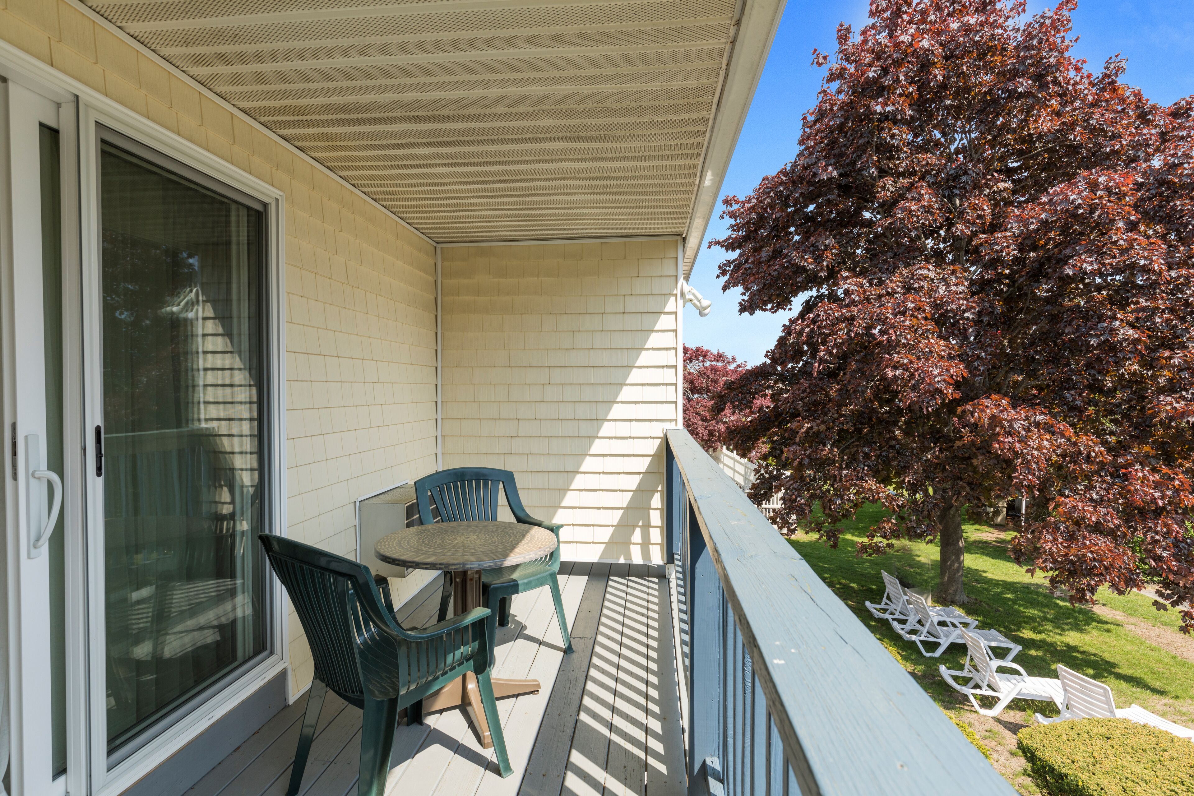 A balcony with a table and chairs, a glass door, and a tree with red leaves.
