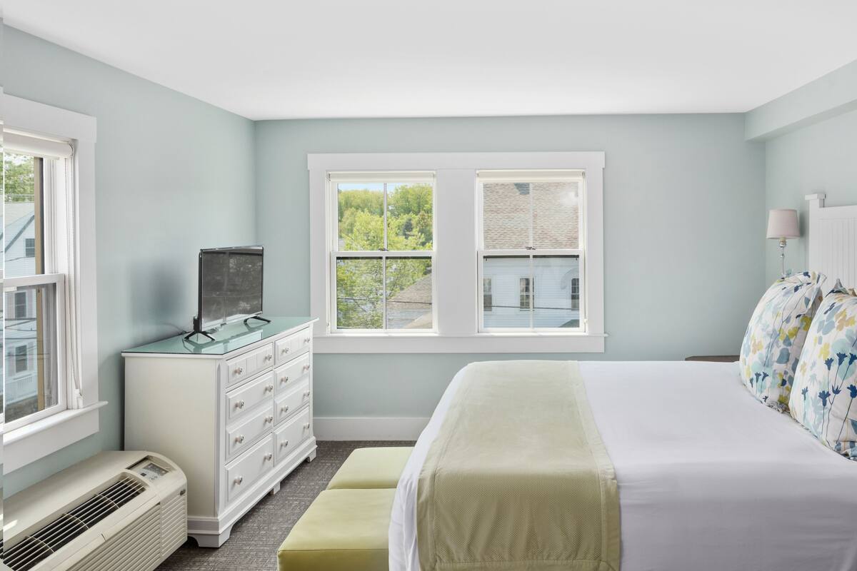 A bedroom with a bed, a dresser, a heater, and a window with a view of trees.