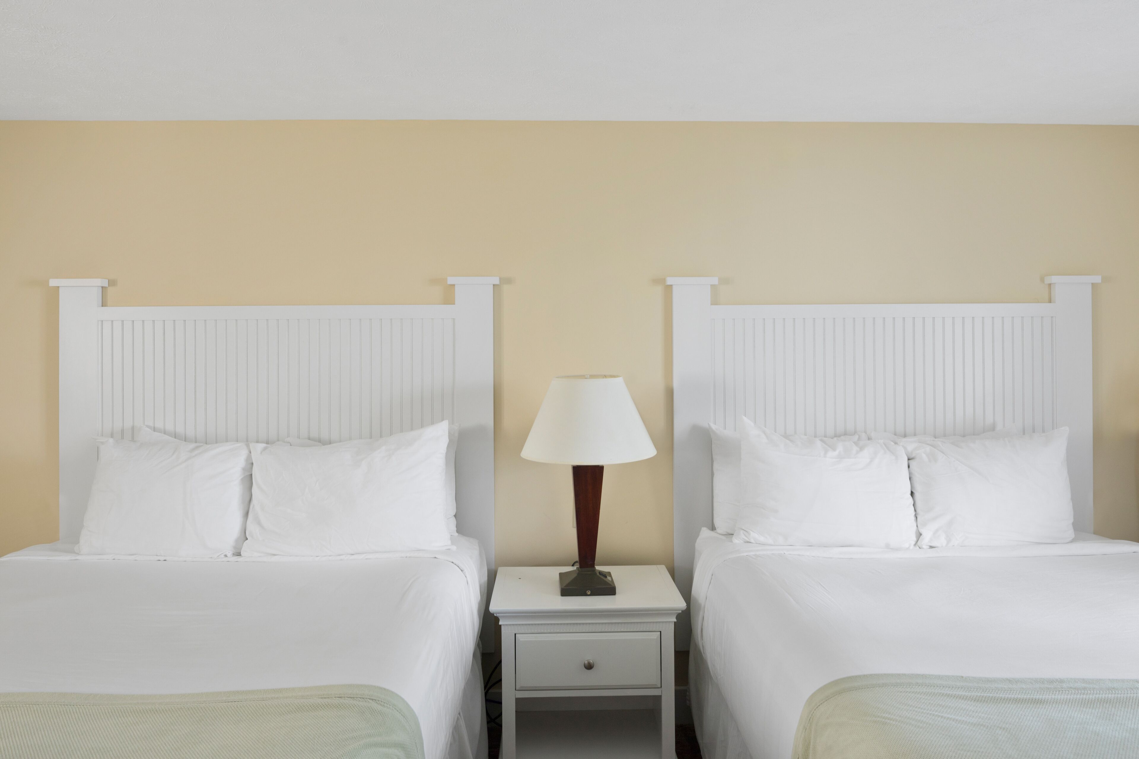 A hotel room with two beds, a nightstand with a lamp, and a small drawer.