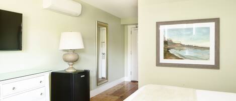 A bedroom with a bed, a dresser, a lamp, a painting, and a door.