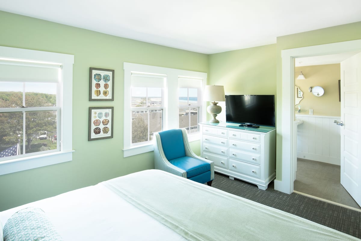 A bedroom with a bed, a chair, a dresser, a television, and a window with a view.