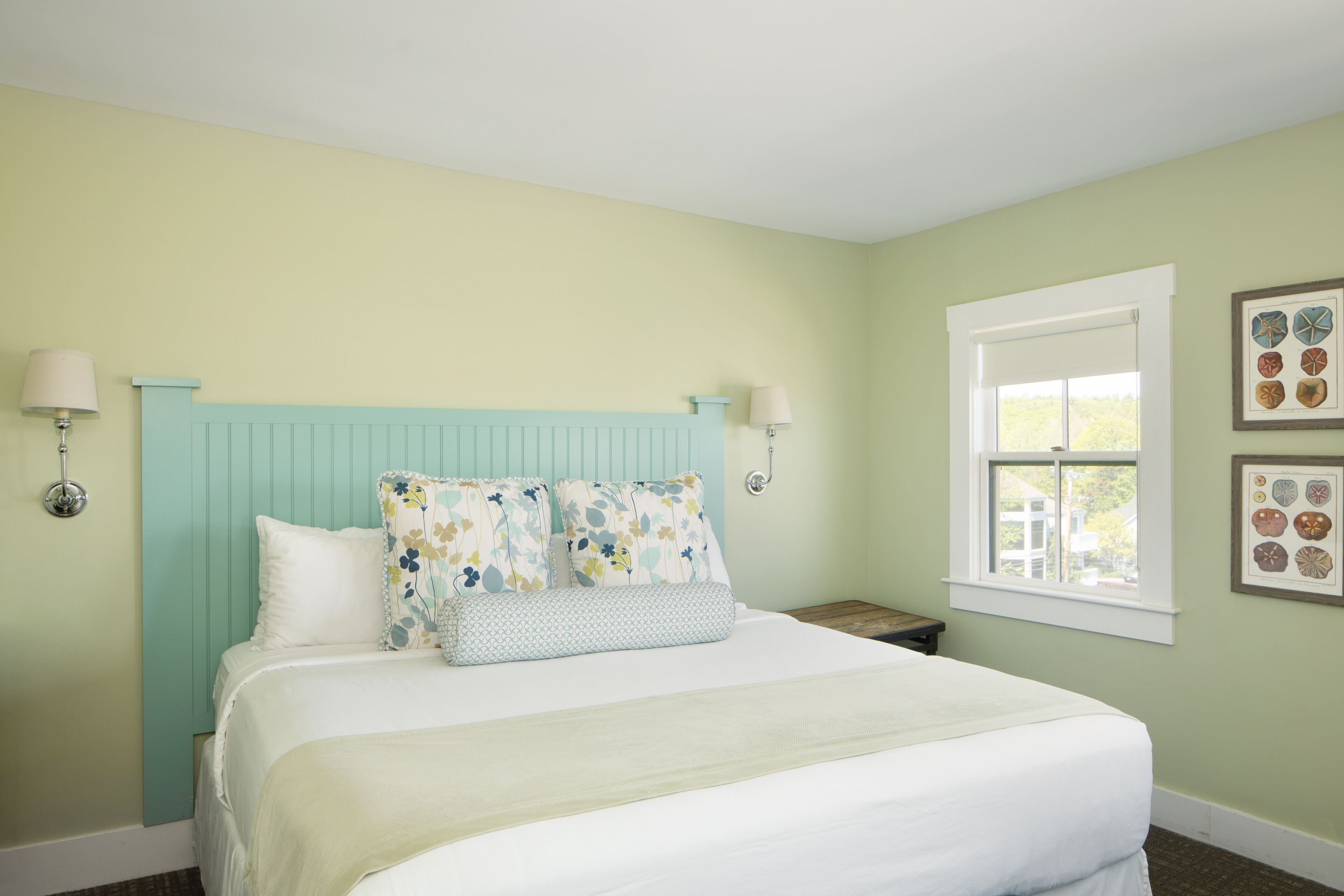 A bedroom with a bed, two bedside tables, a window, and wall art.