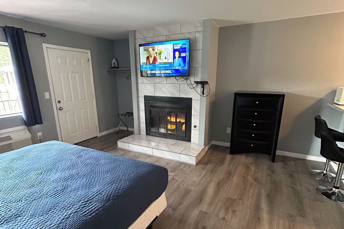 A hotel room with a large bed, a fireplace, a television mounted above it, and a desk with a chair.