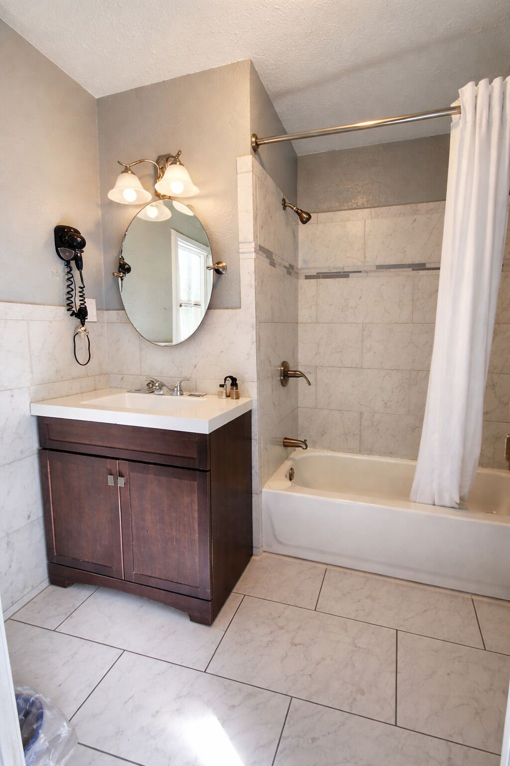 Un baño con tocador, espejo, secador de pelo, ducha con cortina y bañera.