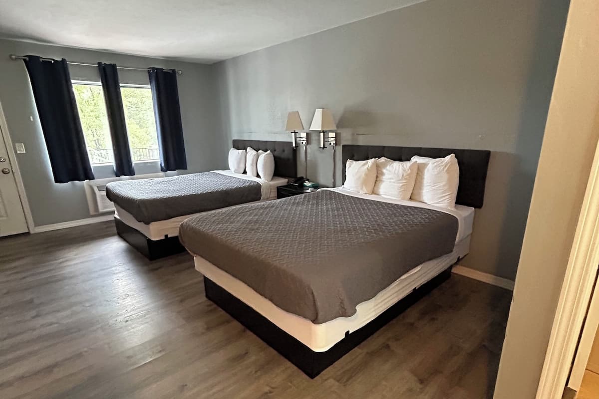 A hotel room with two beds, a nightstand, a lamp, and a window with curtains.