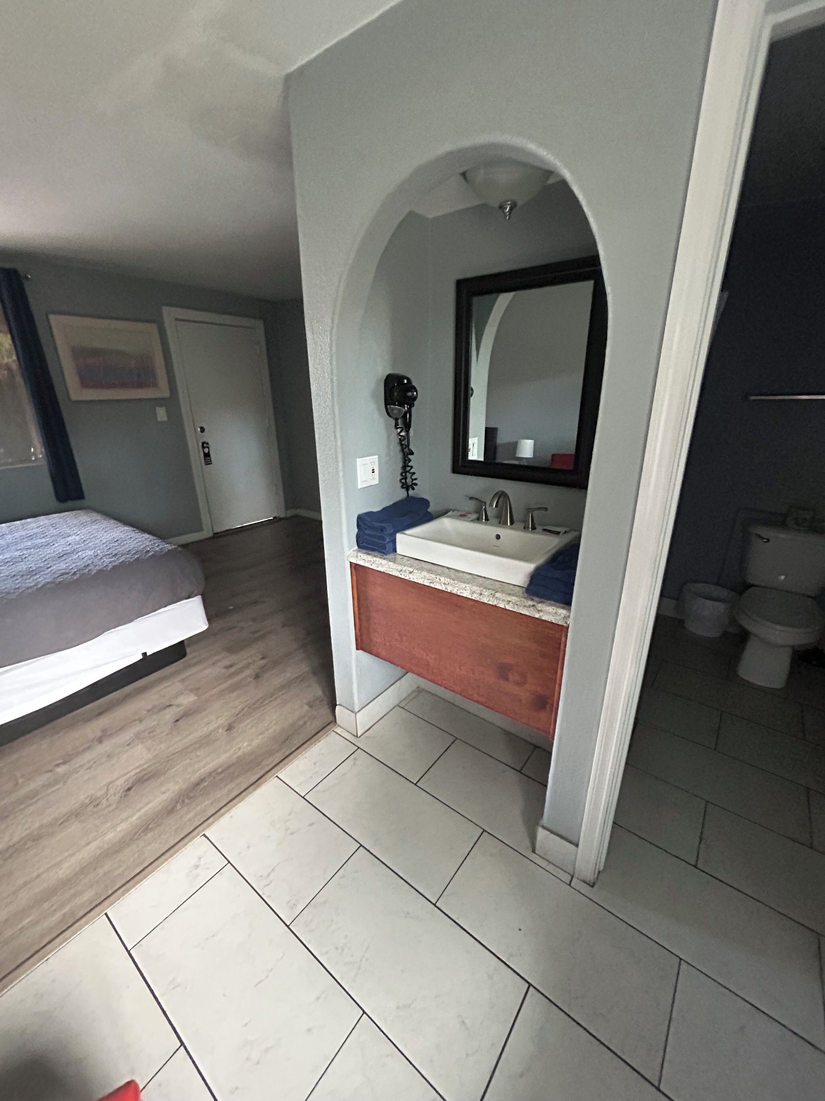Un dormitorio con cama, un baño con lavabo y espejo, y un inodoro.