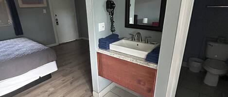 Un dormitorio con cama, un baño con lavabo y espejo, y un inodoro.