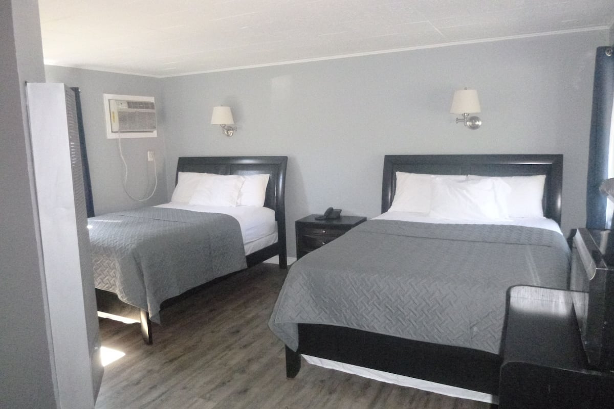 A hotel room with two beds, a desk, a chair, a telephone, and a wall-mounted air conditioning unit.