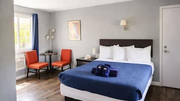 A hotel room with a large bed, two chairs, a small table, and a window with curtains.
