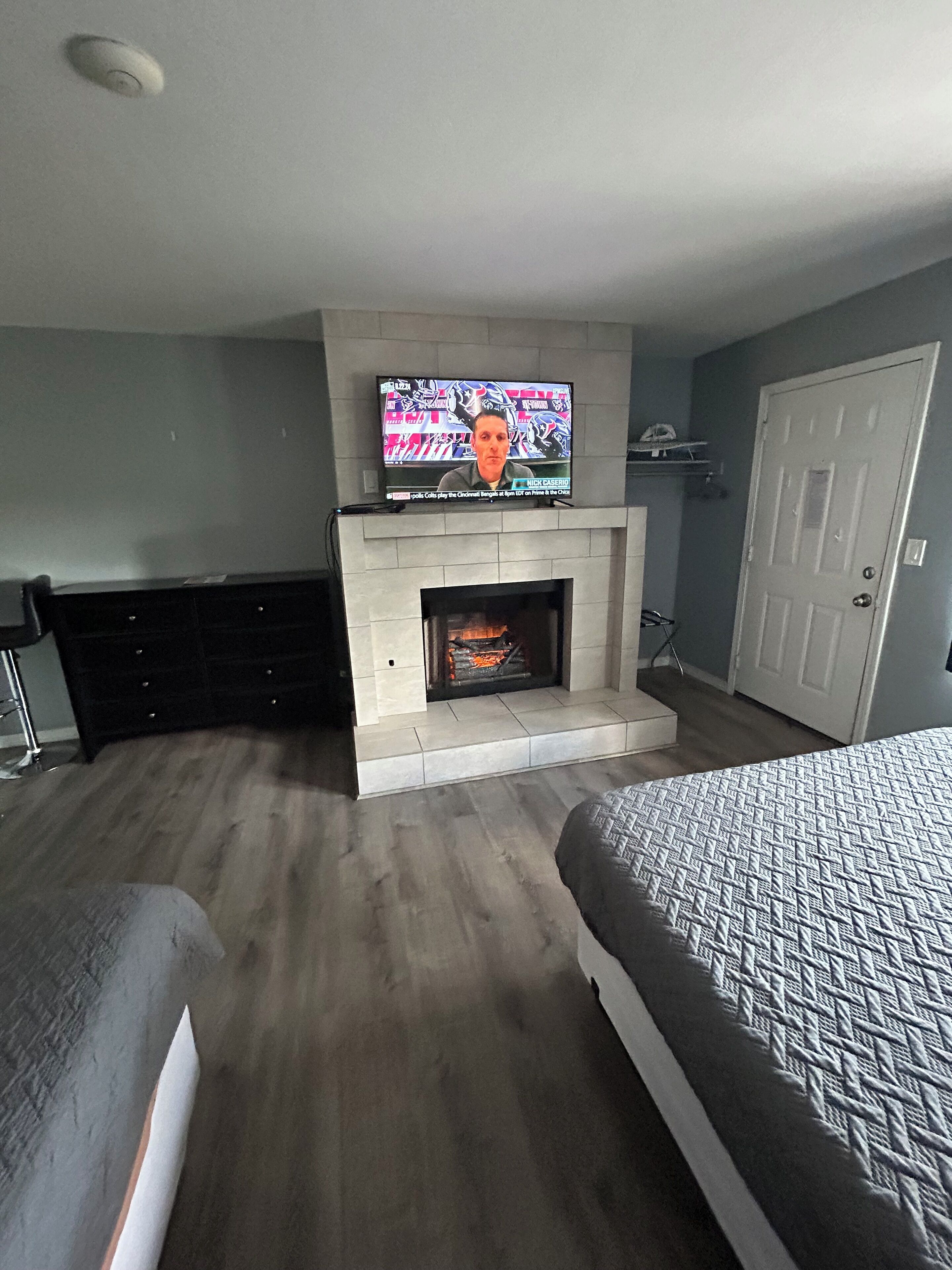 A room with a fireplace, a television mounted above it, a bed, and a door.