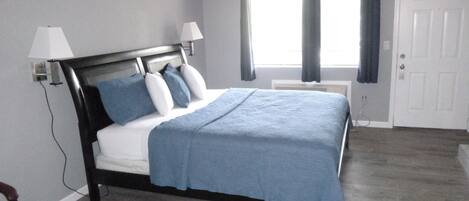 A bedroom with a bed, two bedside lamps, a window with curtains, and a door.