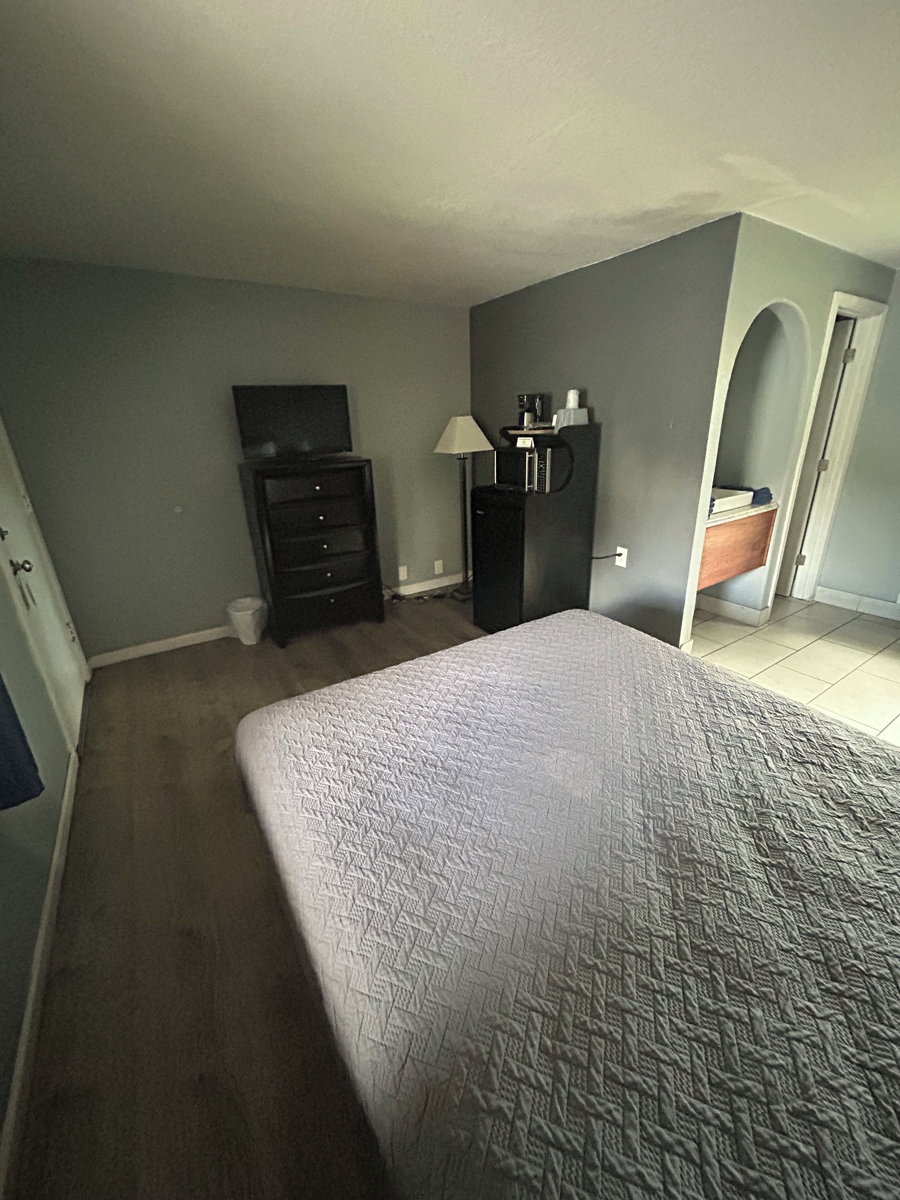 Un dormitorio con cama, cómoda, televisor y escritorio con lámpara.