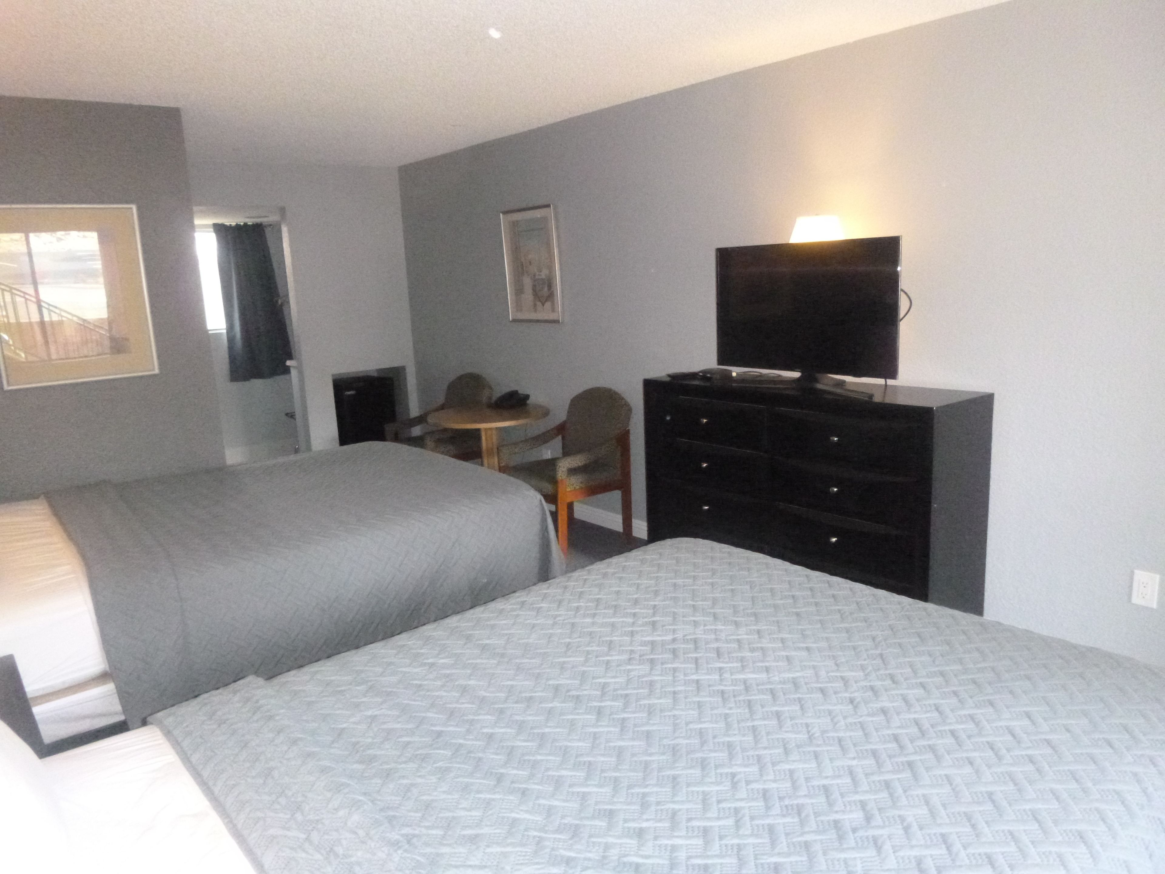 Ein Hotelzimmer mit zwei Betten, einem Schreibtisch, einem Stuhl, einer Kommode und einem Fernseher.