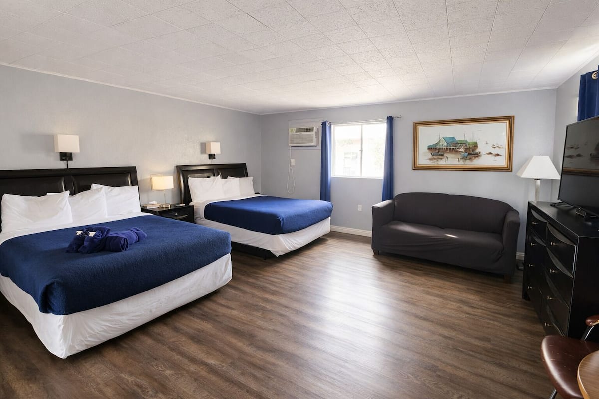 A hotel room with two beds, a sofa, a TV, and a painting on the wall.
