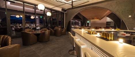 A modern bar area with leather seating, a long counter, and pendant lighting.