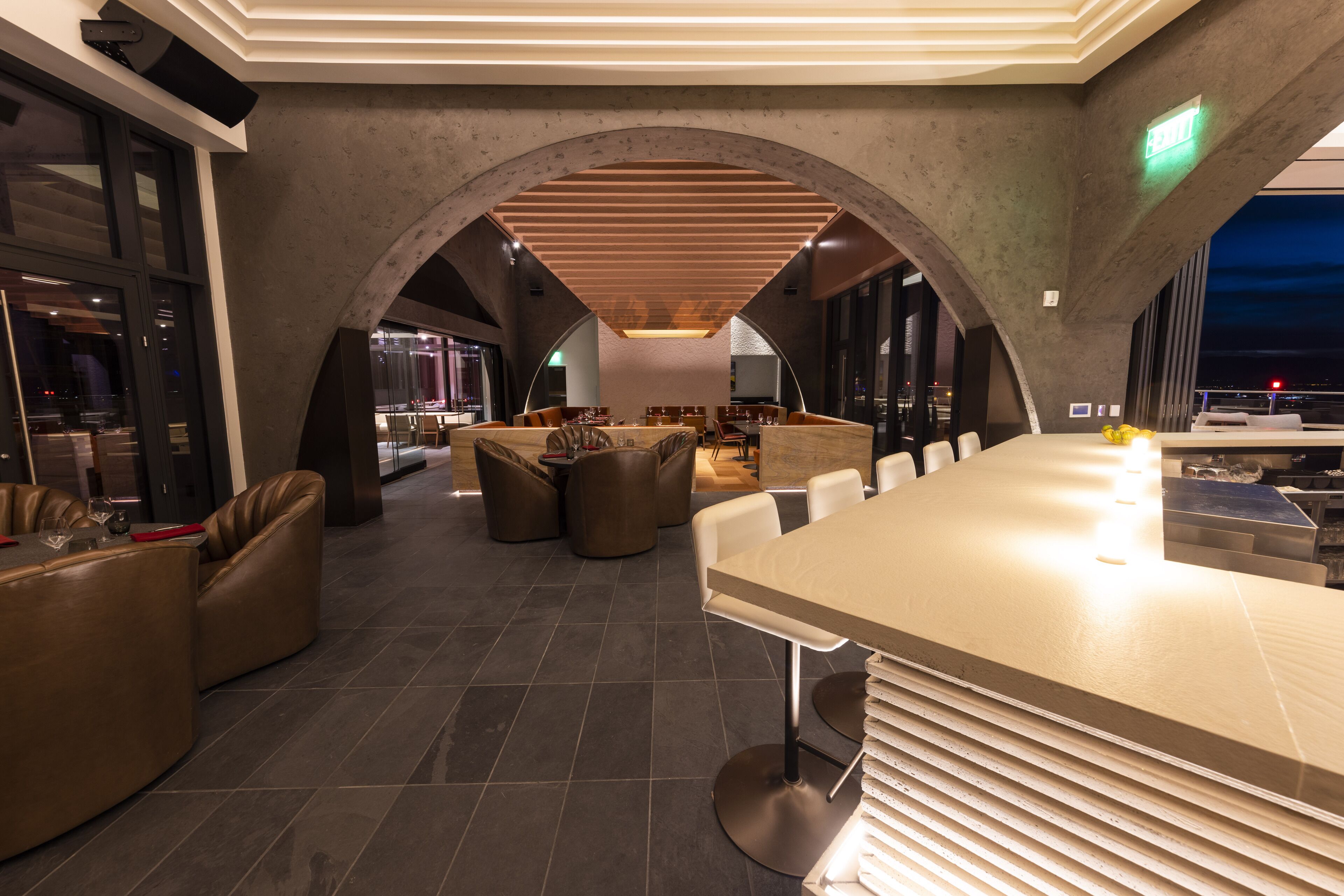 Zona de bar moderna con una barra alargada, asientos de cuero y vistas nocturnas de la ciudad.