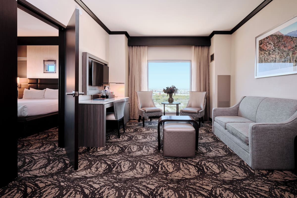 Habitación de hotel con cama, escritorio, dos sillas, sofá, una mesita y un ventanal con vistas.