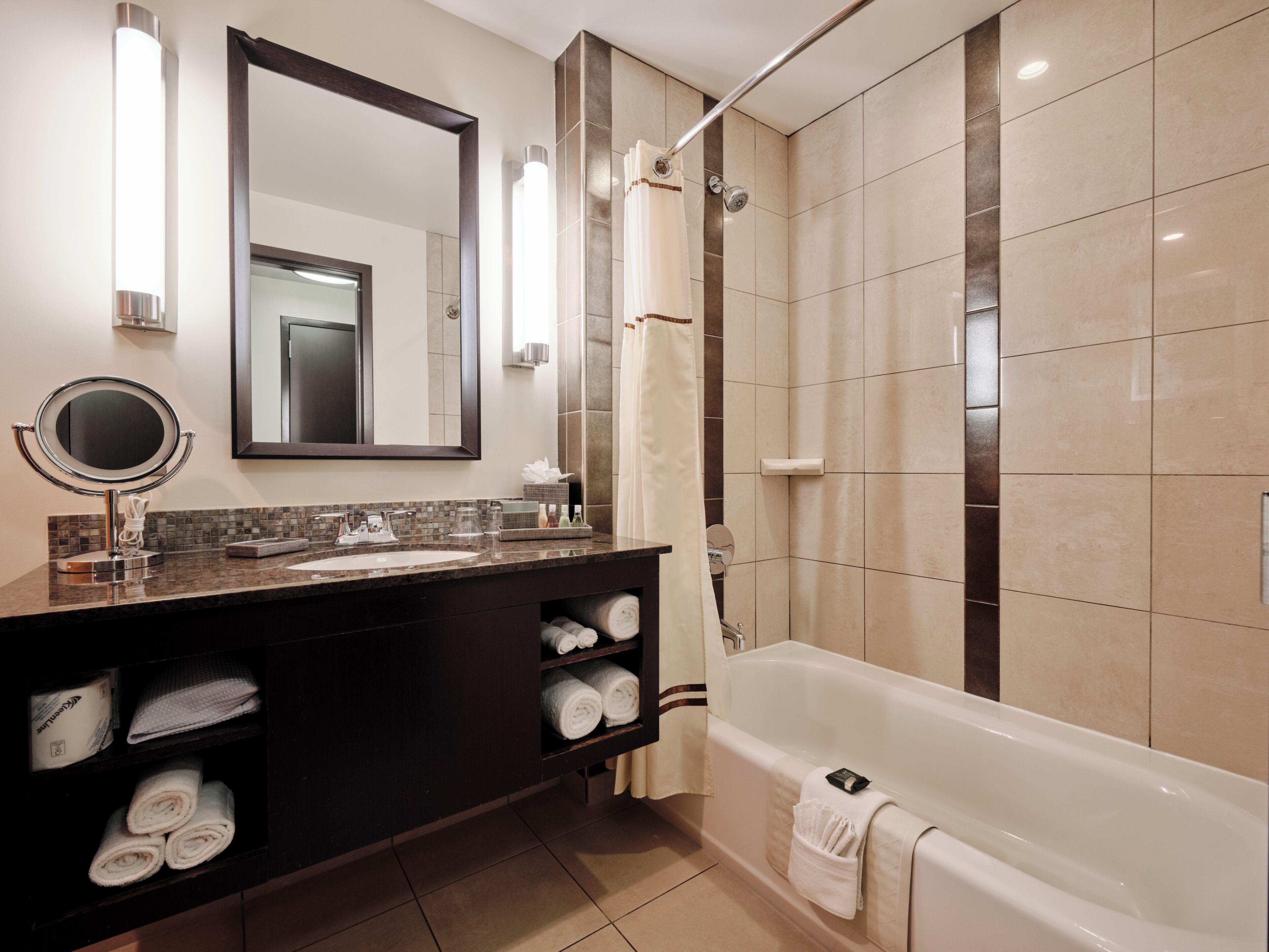 Un baño moderno con un espejo grande, un tocador redondo, una bañera y una zona de ducha.